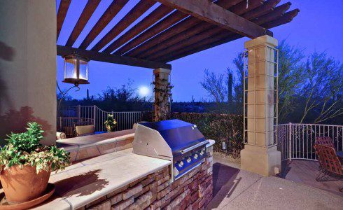 A grill sitting under an outdoor pergola.